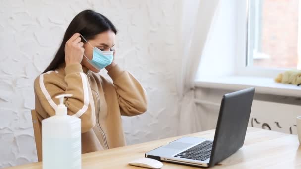 Een jonge vrouw met een beschermend medisch masker deelt ontsmettingsmiddel uit aan de handen tijdens de COVID-19 quarantaine. — Stockvideo