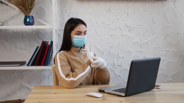 Eine junge Frau in einer medizinischen Schutzmaske und Handschuhen, die während der COVID-19-Quarantäne arbeitet. — Stockvideo