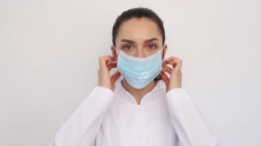 yakın plan gülümseyen doktor kadın hemşire beyaz bir ceket giyiyor, koruyucu bir maske takıyor, kameraya bakıyor.