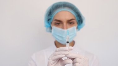 Beyaz önlüklü, şapkalı, koruyucu maskeli hemşire kadın şırıngaya iğne yapıyor.