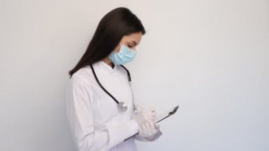 Beyaz önlüklü, koruyucu maskeli, dost canlısı kadın doktor, tanıyı müşteri kartına yazar.,