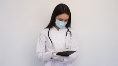 Beyaz önlüklü, koruyucu maskeli, dost canlısı kadın doktor, tanıyı müşteri kartına yazar.,