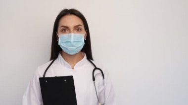 Beyaz önlüklü, koruyucu maskeli, elinde müşteri kartı olan dost canlısı bir doktor.,