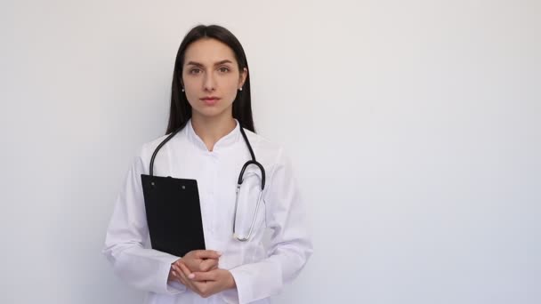 Dost canlısı bayan doktor elinde bir dosya, boynunda bir steteskop tutarak gülümsüyor. — Stok video