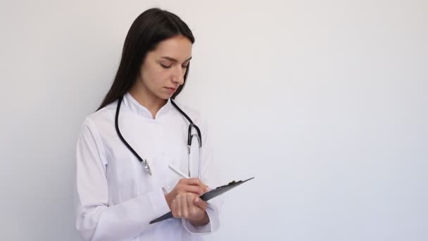 Femme médecin amicale, écrit le diagnostic à la carte des clients, un stéthoscope sur son cou — Video