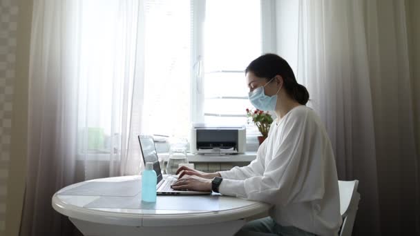 认真的年轻女性自由职业者 戴着医疗防护面具 从家里工作 在笔记本电脑上输入电子邮件 专心致志的女孩坐在椅子上上网学习 被隔离的女孩19 — 图库视频影像