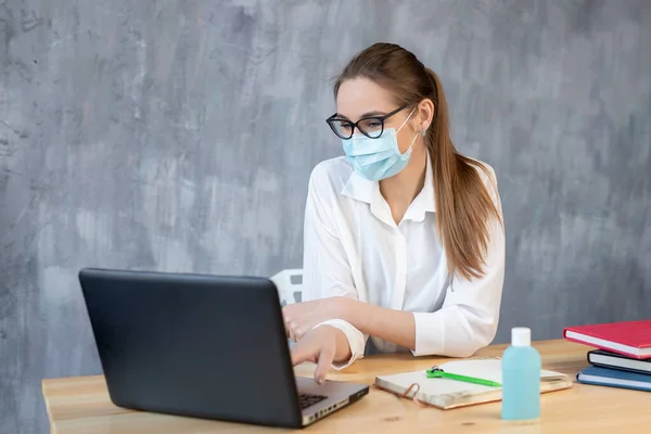 Coronavirus. Koruyucu maske takarak evden çalışan genç bir iş kadını. Koronavirüs için karantinada koruyucu maske takan bir iş kadını. Evde dezenfektan jeliyle çalışıyor..