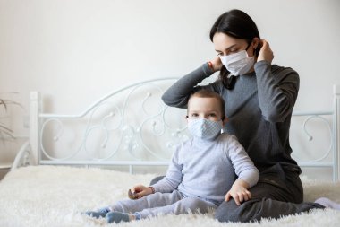 Tıbbi koruyucu maskeli küçük bir çocuk. Anne, bebek steril tıbbi maskesini takıyor. Çocuk, yüz maskesi takıyor