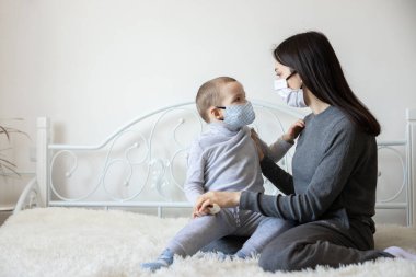 Tıbbi koruyucu maskeli küçük bir çocuk. Anne, bebek steril tıbbi maskesini takıyor. Çocuk, yüz maskesi takıyor