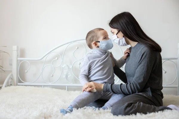 Tıbbi koruyucu maskeli küçük bir çocuk. Anne, bebek steril tıbbi maskesini takıyor. Çocuk, yüz maskesi takıyor