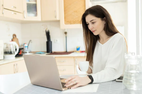 Genç öğrenci dizüstü bilgisayarla e-öğreniyor ve mutfakta kahve içiyor. Öğrenci sanal öğretmenle çevrimiçi çalışıyor ve yeni dersler öğreniyor. E-öğrenim eğitim kavramı