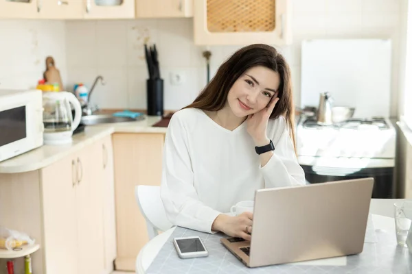 Evde dizüstü bilgisayarla çalışan gülümseyen kız. Evdeki serbest çalışan genç kız metin yazarı. Uzaktan çalışma konsepti. Kamerada göster
