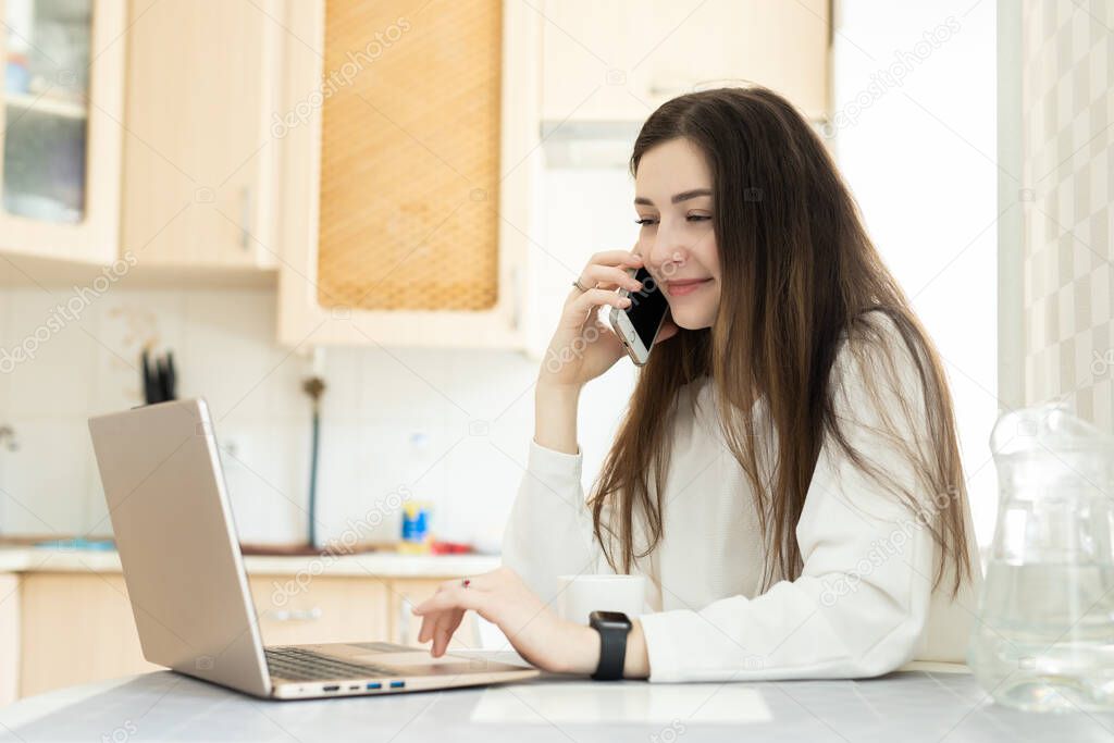Smiling freelancer consults by cell phone at home. The young girl freelancer copywrite from home. Remote working and telephone consultations concept