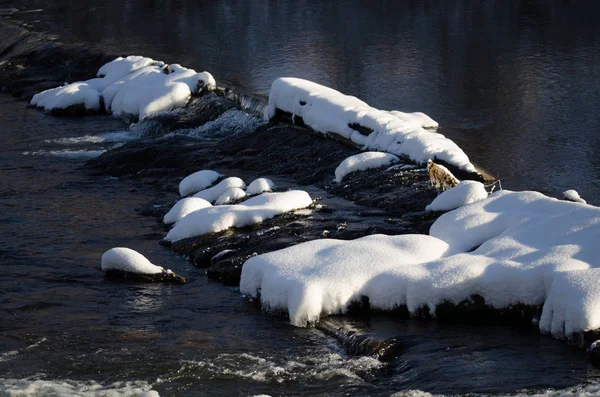 Rochas cobertas de neve formando barragem do outro lado do rio frio de inverno — Fotografia de Stock