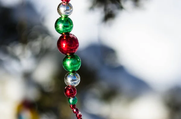 Rote, grüne und silberne Weihnachtsschmuckperlen schmücken einen verschneiten Baum im Freien — Stockfoto