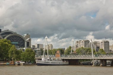 Bulutlu bir yaz gününde Londra Thames nehrinin güney kıyısından Golden Jubilee Köprüleri ve Charing Cross İstasyonu manzarası.