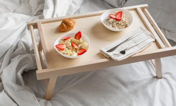 European breakfast in bed: oatmeal, banana, strawberry,  croissant. Copy space. Horizontal orientation. High key.