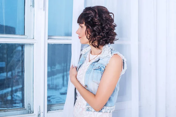 Young beautiful woman standing and waiting sad looking out the window. — Stock Photo, Image