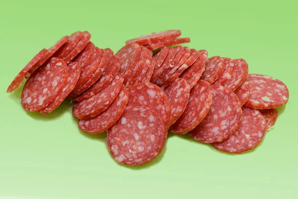 Sliced smoked sausage on a green background — Stock Photo, Image