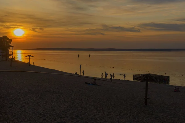 Solnedgang over en flod strand med vacationers - Stock-foto