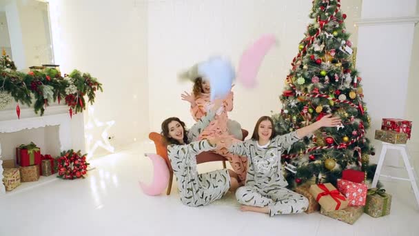 Три девушки веселятся в пижаме рядом с елкой — стоковое видео