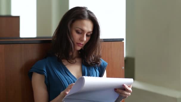 Prores. Una joven con un vestido azul está estudiando material educativo en el público — Vídeo de stock