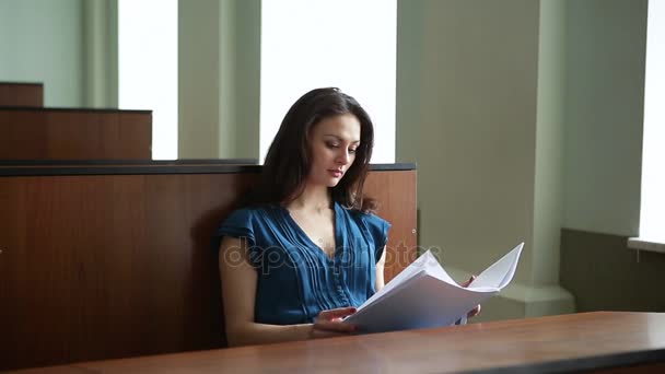 Prores. Una joven con un vestido azul está estudiando material educativo en el público — Vídeos de Stock