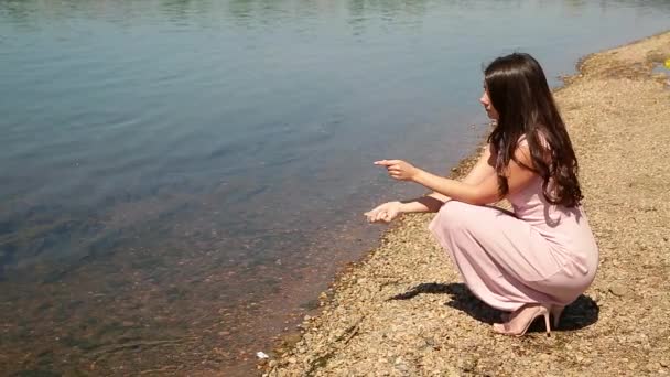 一个穿着粉红色连衣裙的浪漫女孩漫步在河里扔石头 — 图库视频影像
