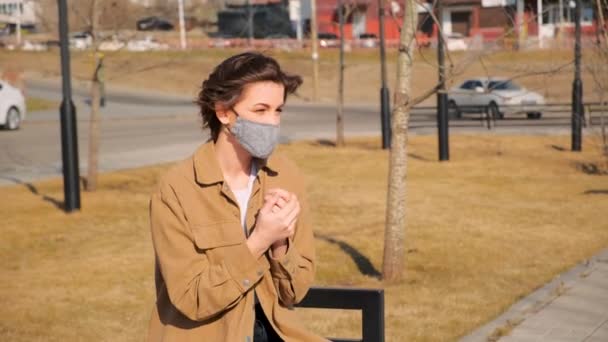 在城市公园里 身穿棕色衣服 脸上戴着医疗面具的年轻女子用红色气球消毒双手 — 图库视频影像