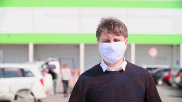 ショッピングセンターや駐車場を背景に顔から医療用マスクを脱いだ男の肖像画 — ストック動画