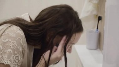 Uzun siyah saçlı, parlak elbiseli genç esmer kız banyoda eğleniyor ve dişlerini fırçalıyor.