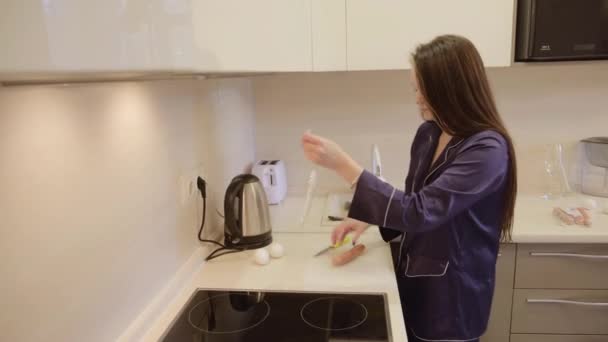 身穿蓝色长发黑发衣服的女孩在公寓厨房里准备煎蛋和香肠 — 图库视频影像