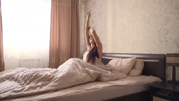 寝室の大きなベッドの上で目を覚ますと窓のカーテンを開けています — ストック動画