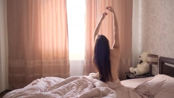 一头乌黑的长发的年轻的赤身裸体女孩在卧室的一张大床上醒来 — 图库视频影像