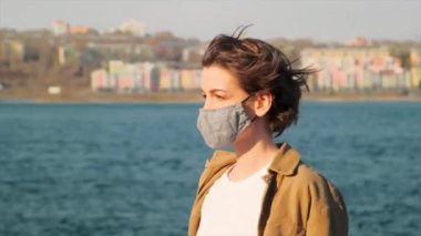 Kahverengi elbiseli genç bir kadın şehir ve nehir geçmişinde tıbbi bir maskeyi çıkartıyor.
