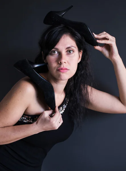 Retrato de foto divertida de modelo de pelo oscuro en vestido negro sobre su hombro con tacones altos tuflemi en la cabeza — Foto de Stock