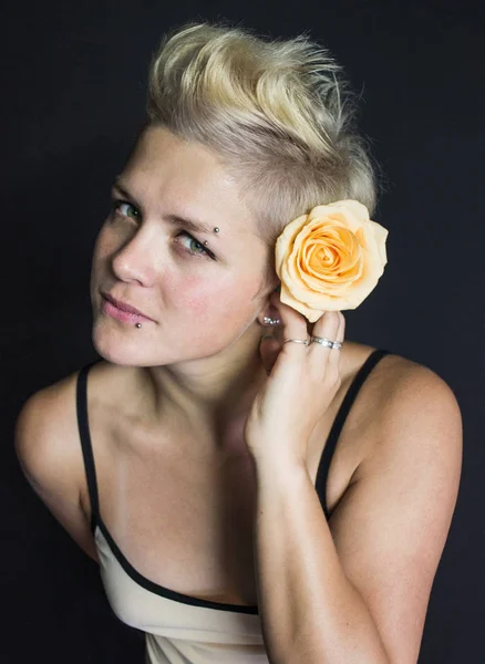 Foto retrato de una rubia de pelo corto con una rosa en el pelo con piercing en el labio y las cejas — Foto de Stock