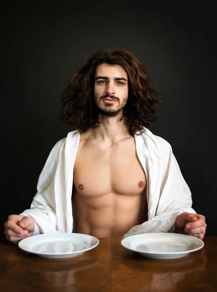 half naked handsome guy with long curly hair at the table with two white empty plates Photo