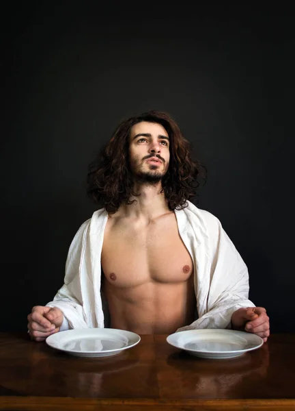 photo guy with long curly hair white drapery and two empty plates looking up in prayer