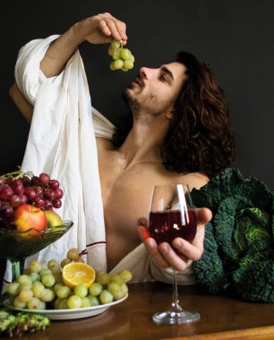 photo half naked curly guy at a table with fruits and wine eating grapes clipart