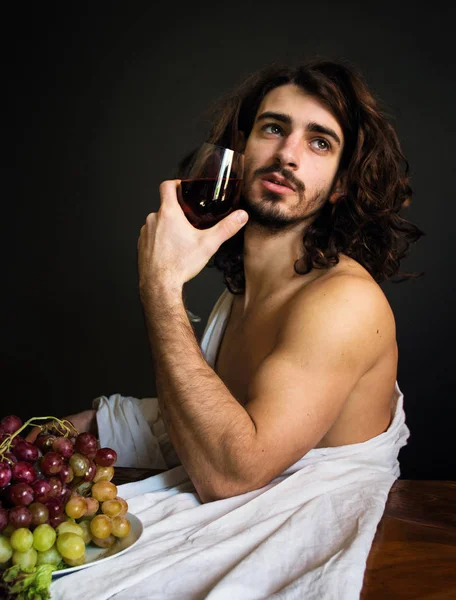 photo half naked curly guy at the table with a plate of grapes and a glass of red drink