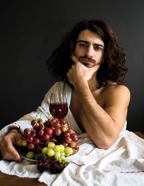 Foto medio desnudo dour rizado chico en la mesa con un plato de uvas y una copa de vino — Foto de Stock