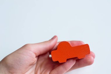 Beyaz arka planda bir el, turuncu bir oyuncak araba tutuyor.