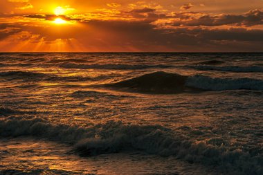 Bulutlu gökyüzü ve yüksek sörflü deniz manzaralı gün batımı