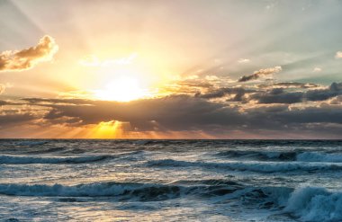 Bulutlu gökyüzü ve yüksek sörflü deniz manzaralı gün batımı