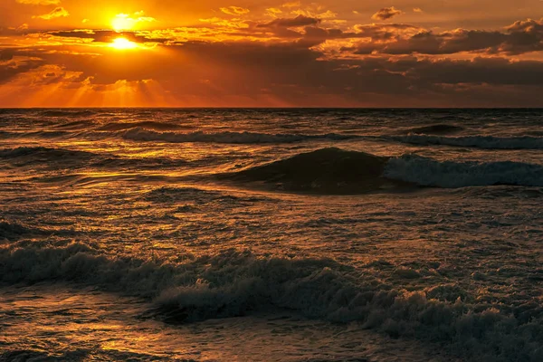 Bulutlu gökyüzü ve yüksek sörflü deniz manzaralı gün batımı