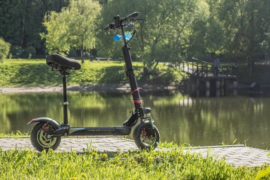 Parkta sıcak bir yaz gününde gölete karşı siyah elektrikli scooter.