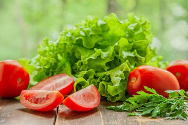 Bahçede yetişen taze kıvırcık marul ve sulu olgun domatesler pencereye karşı ahşap bir masada.