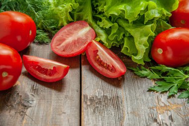 Bahçede yetişen taze kıvırcık salata ve ahşap bir masada sulu olgun domatesler.
