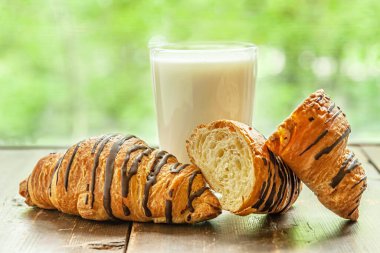 Taze pişmiş kruvasan ve bir bardak taze organik süt pencerenin yanındaki ahşap masada.